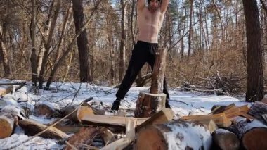 Güneşli bir kış ormanında yakacak odun kesen üstsüz, güçlü bir adam. Karlı ormanlık alanda baltayla çalışan kaslı bir adam. Güç kavramı, erkeksi, enerji ve soğuk mevsim boyunca doğayla uyum..