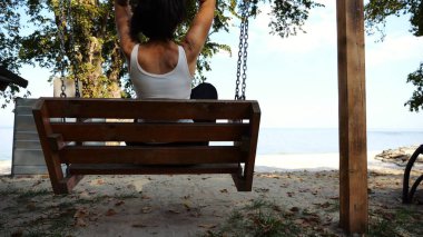 Mutlu kadın deniz sahillerinde salıncakta sallanıyor. Kaygısız kadın okyanus kenarında dinleniyor. Yetişkin bir kadın güneşli bir günde deniz kıyısında eğleniyor. Yaz tatili ya da tatil kavramı. Yavaş çekim