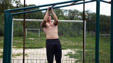 Genç kaslı sporcu spor alanında barfiks çekiyor. Atletik adam dışarıda egzersiz yapıyor. Yaz doğasında spor yapan güçlü bir adam. Sağlıklı ve aktif yaşam tarzı kavramı. Yavaş çekim