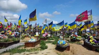 View from window of moving automobile on large military cemetery in Kharkiv with countless graves marked by Ukrainian flags. The site commemorates soldiers who died during russian invasion in Ukraine.