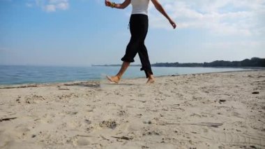 Güneşli bir günde sahilde kumsala giden mutlu yetişkin kadın. Arka planda sakin dalgalarla deniz kıyısında yürüyen güzel bir bayan. Yaz tatili ya da tatil kavramı. Yavaş çekim