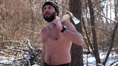 Tişörtsüz sakallı adamın portresi karlı bir kış ormanında baltayla duruyor. Karlı korulukta odun kestikten sonra dinlenen yorgun adam. Sahne soğuk koşullarda açık havada çalışmayı temsil ediyor..