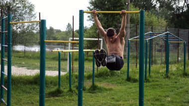 Atletik adam karın kaslarını eğitir spor sahasında yatay barda bacak kaldırır. Genç sporcu, barfiks çekme çubuğunda egzersiz yapıyor. Doğada spor yapan sporcu. Sağlıklı yaşam tarzı.
