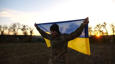 Üniformalı genç bir erkek asker Ukrayna bayrağını kaldırdı. Ukrayna ordusunun askeri, Rus saldırısına karşı zafer sembolü olarak mavi-sarı bayrağı kaldırdı..