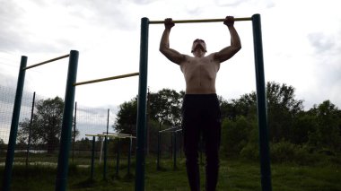 Spor sahasında barfiks çeken kaslı bir sporcu. Genç üstsüz sporcu doğada egzersiz yapıyor. Güçlü sporcu adam dışarıda antrenman yapıyor. Sağlıklı ve aktif yaşam tarzı kavramı. Yavaş çekim