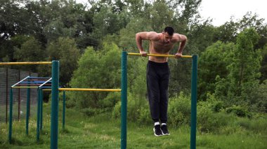 Cesur üstsüz sporcu doğada yatay çıtada şınav çekiyor. Güçlü ve kaslı adam spor alanında antrenman yapıyor. Genç atletik adam dışarıda egzersiz yapıyor. Aktif ve sağlıklı yaşam tarzı kavramı.