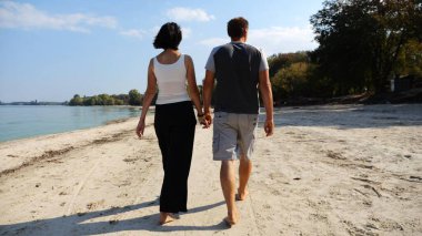 Romantik çift el ele tutuşup kıyı şeridinde yürüyor. Güneşli bir günde deniz kıyısına giden mutlu bir çift. Sevgililer tatil köyünde birlikte vakit geçirirler. Tatil ya da tatil kavramı. Yavaş çekim