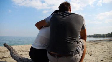 Kumsalda tahta kütüğün üzerinde otururken mutlu çift kucaklaşması. Güneşli bir günde deniz manzarasına hayran olan romantik bir çift. Sevgililer tatil köyünde birlikte vakit geçirirler. Yaz tatili ya da tatil kavramı. Yavaş çekim