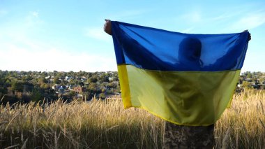 Üniformalı bir asker, Ukrayna bayrağının üzerinde kırsalda dikiliyor. Rus saldırısına karşı kazanılan zaferin şerefine ulusal bayrağı kaldıran Ukraynalı erkek asker. Savaşın sonu..