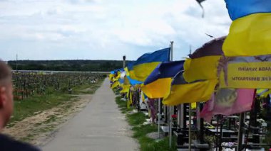 Mourning man go among countless graves of ukrainian soldiers with national flags at military cemetery in Kharkiv. Scene reflects personal sorrow and nation collective loss caused by russian aggression.