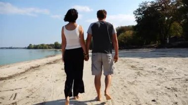 Romantik çift el ele tutuşup kıyı şeridinde yürüyor. Güneşli bir günde deniz kıyısına giden mutlu bir çift. Sevgililer tatil köyünde birlikte vakit geçirirler. Tatil ya da tatil kavramı. Yavaş çekim