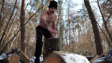 Kaslı bir adam kış ormanındaki bir kütüğe kütük yerleştiriyor. Gömleksiz genç adam karlı ormanlık alanda yakacak odun kesmeye hazırlanıyor. Soğuk mevsimde doğayla enerji ve uyum kavramı.