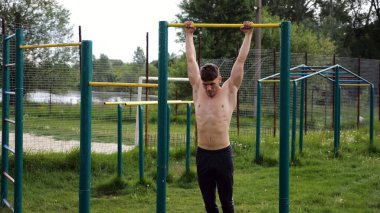 Spor sahasında barfiks çeken kaslı bir sporcu. Genç üstsüz sporcu doğada egzersiz yapıyor. Güçlü sporcu adam dışarıda antrenman yapıyor. Sağlıklı ve aktif yaşam tarzı kavramı. Yavaş çekim