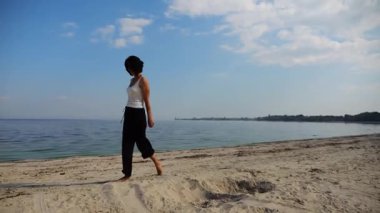 Güneşli bir günde sahilde kumsala giden mutlu yetişkin kadın. Arka planda sakin dalgalarla deniz kıyısında yürüyen güzel bir bayan. Yaz tatili ya da tatil kavramı. Yavaş çekim