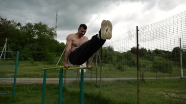 Güçlü bir adam karın kaslarını eğitir spor sahasında paralel barlarda bacak kaldırır. Genç üstsüz sporcu doğada egzersiz yapıyor. Doğada spor yapan sporcu. Sportif yaşam tarzı kavramı.