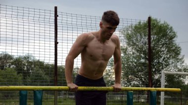 Erkek üstsüz sporcu doğada paralel barlarda şınav çekiyor. Spor alanında egzersiz yapan güçlü bir sporcu. Genç sporcu dışarıda sıkı çalışıyor. Aktif spor yaşam tarzı kavramı. Yavaş çekim