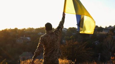 Ukrayna ordusunun genç askeri gün batımında Rus saldırısına karşı kazanılan zaferin şerefine mavi-sarı bayrak kaldırdı. Üniformalı erkek ordu kırsal kesimde Ukrayna bayrağı salladı..