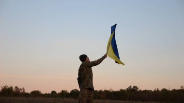 Erkek asker, Rusya 'nın işgal ettiği özgür bölgede mavi-sarı bayrak sallıyor. Ukrayna ordusunun genç askeri, hava kararırken Rus saldırısına karşı kazanılan zaferin şerefine Ukrayna bayrağı kaldırdı..