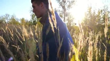 Üniformalı genç bir erkek asker kırsalda mavi-sarı pankartla geziyor. Ukrayna ordusunun askeri Rus saldırısına karşı zafer sembolü olarak ulusal bayrağıyla yürüyor..