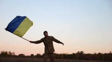 Erkek asker, Rusya 'nın işgal ettiği özgür bölgede mavi-sarı bayrak sallıyor. Ukrayna ordusunun genç askeri, hava kararırken Rus saldırısına karşı kazanılan zaferin şerefine Ukrayna bayrağı kaldırdı..