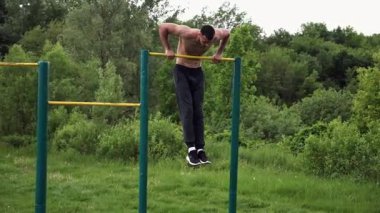 Güçlü ve kaslı bir adam doğanın yatay çubuğunda egzersiz yapıyor. Spor sahasında sıkı gömleksiz sporcu. Genç atletik adam dışarıda egzersiz yapıyor. Sağlıklı yaşam tarzı kavramı.