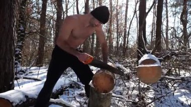 Gömleksiz bir adam güneşli kış ormanında odun kesiyor. Karlı ormanlık alanda birlikte çalışan güçlü bir adam. Sahne, soğuk koşullarda insan çabalarının ve açık hava faaliyetlerinin altını çiziyor. Yavaş çekim