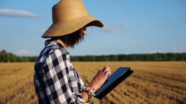 Yetişkin çiftçi güneşli bir günde buğday çayırında dijital tablet kullanıyor. Kadın tarım uzmanı arpa tarlasında hasat gözlemliyor. Güzel manzara manzarası. Tarım sektörü kavramı. Yavaş çekim