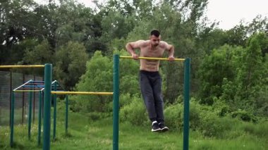 Güçlü ve kaslı bir adam doğanın yatay çubuğunda egzersiz yapıyor. Spor sahasında sıkı gömleksiz sporcu. Genç atletik adam dışarıda egzersiz yapıyor. Sağlıklı yaşam tarzı kavramı.