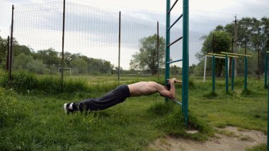 Spor malzemelerinde trisepsler üzerinde egzersiz yapan genç kaslı bir atlet. Spor alanında spor yapan erkek üstsüz bir sporcu. Doğada güçlü bir sporcu eğitimi. Sağlıklı yaşam tarzı kavramı.