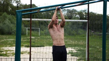 Genç kaslı sporcu spor alanında barfiks çekiyor. Atletik adam dışarıda egzersiz yapıyor. Yaz doğasında spor yapan güçlü bir adam. Sağlıklı ve aktif yaşam tarzı kavramı. Yavaş çekim