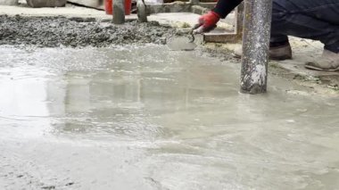 Koruyucu eldivenli erkek eller, bahçeye taze çimento serpmek ve düzleştirmek için mala kullanır. Malzeme, beton tabakaya dönüşmeden önce hazırlık çalışmalarının bir parçası olarak dikkatlice yüzeye uygulanır..