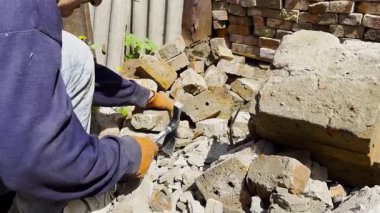 Koruyucu eldivenli erkek eller, tadilat sırasında kullanılmış tuğlalardan eski çimentoyu çıkarmak için çekiç kullanır. İşlem, tuğla yüzeyini yeniden inşaata hazırlamak için dikkatlice temizlemeyi içeriyor..