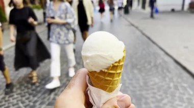 Şehir caddesinde yürürken erkek elin dondurma külahını tuttuğu pov. Bulanık yayalar arka plandan geçerek canlı bir şehir atmosferi yaratıyor ve kol tedavisini vurguluyorlar..