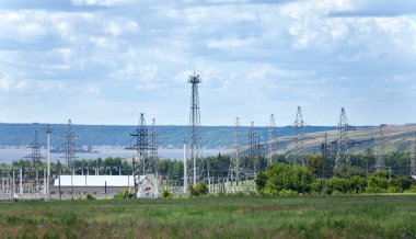 Yaz manzarası resimli tarlalar, çayırlar ve içinden geçen elektrik hatları.