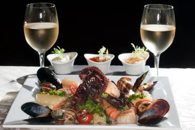 Macro, beyaz tabak, deniz ürünleri ve şarap bardaklarıyla beyaz şarap, siyah arka plandaki bir stüdyoda beyaz bir masa örtüsü.