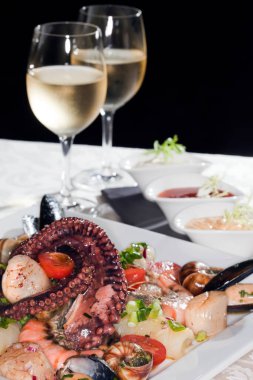 Macro, beyaz tabak, deniz ürünleri ve şarap bardaklarıyla beyaz şarap, siyah arka plandaki bir stüdyoda beyaz bir masa örtüsü.