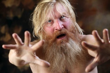 Sakallı ve bıyıklı çıplak bir adamın yakın plan portresi, güçlü duygularını ifade ediyor, kahverengi arka planda stüdyo.