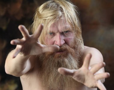 Sakallı ve bıyıklı çıplak bir adamın yakın plan portresi, güçlü duygularını ifade ediyor, kahverengi arka planda stüdyo.