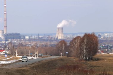 Şehre giden otoyolun insan yapımı manzarası ve ilkbaharın başında ufukta sigara içilen bacaları olan bir termik santral.