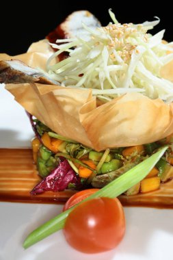 Siyah arka plan stüdyosunda hamurdan yapılmış bir sepetin içinde balık ve sebzeli yakın plan gurme salatası.