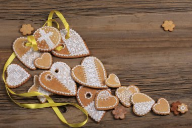  Sarı kurdeleli kalp şeklinde makro zencefilli kurabiye, ahşap arka planda çiçekler.