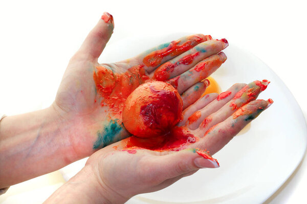 close-up of a single egg in the orange paint in female hands on a light background studio