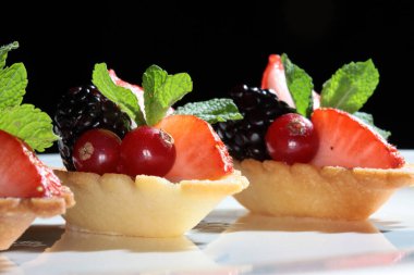 Koyu bir arka plan stüdyosunda çilek ve böğürtlenli lezzetli bir pasta.