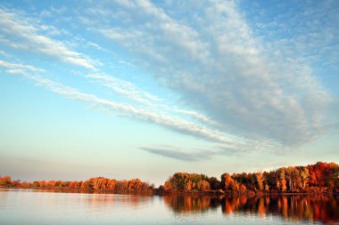 Sonbahar manzarası nehirde güzel bir sabah kumsalda renkli ağaçlar ve mavi gökyüzünde bulutlar.