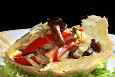 Siyah arka plan stüdyosundaki beyaz tabakta hamurdan yapılmış sepetin içinde mantarlı makro sebze salatası.