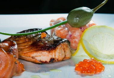 Kızarmış balık, havyar, limon, koyu arkaplanda kiraz domatesleri ve kapari stüdyolarıyla süslenmiş makro lezzetli bir yemek.