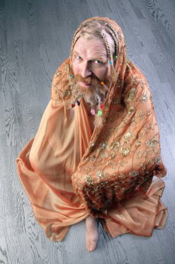 Uzun sakallı, bıyıklı, örgülü saçı örgülü bej bir fular stüdyosuna sarılıp açık arkaplanlı bir nilüfer ağacına sarılmış bir adamın portresi.