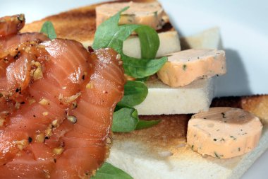 Kızarmış ekmek, füme kırmızı balık ve beyaz tabak stüdyosunda yeşillikler.