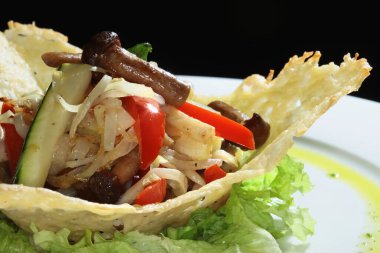 Siyah arka plan stüdyosundaki beyaz tabakta hamurdan yapılmış sepetin içinde mantarlı makro sebze salatası.