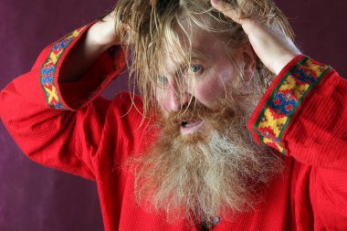 Kırmızı gömlek stüdyosunda uzun sakallı, bıyıklı ve ıslak sarı saçlı kutsanmış birinin yakın plan portresi.